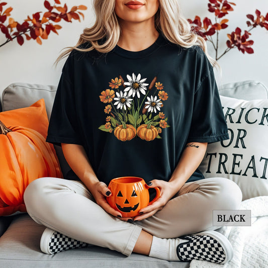 Person wearing a black t-shirt with pumpkins and flowers design, holding an orange mug, sitting on a couch with Halloween-themed decor.