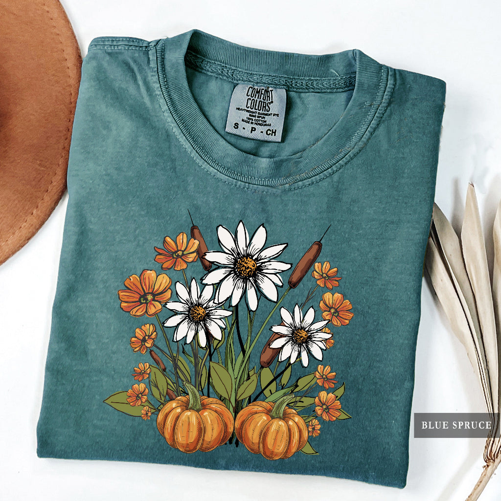 Folded teal t-shirt with floral and pumpkin design on a white background