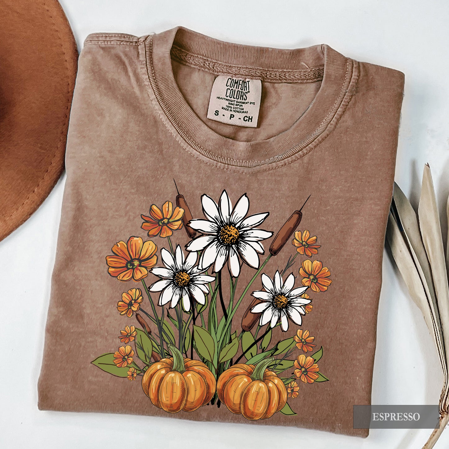 Folded brown t-shirt with floral and pumpkin design on a white background