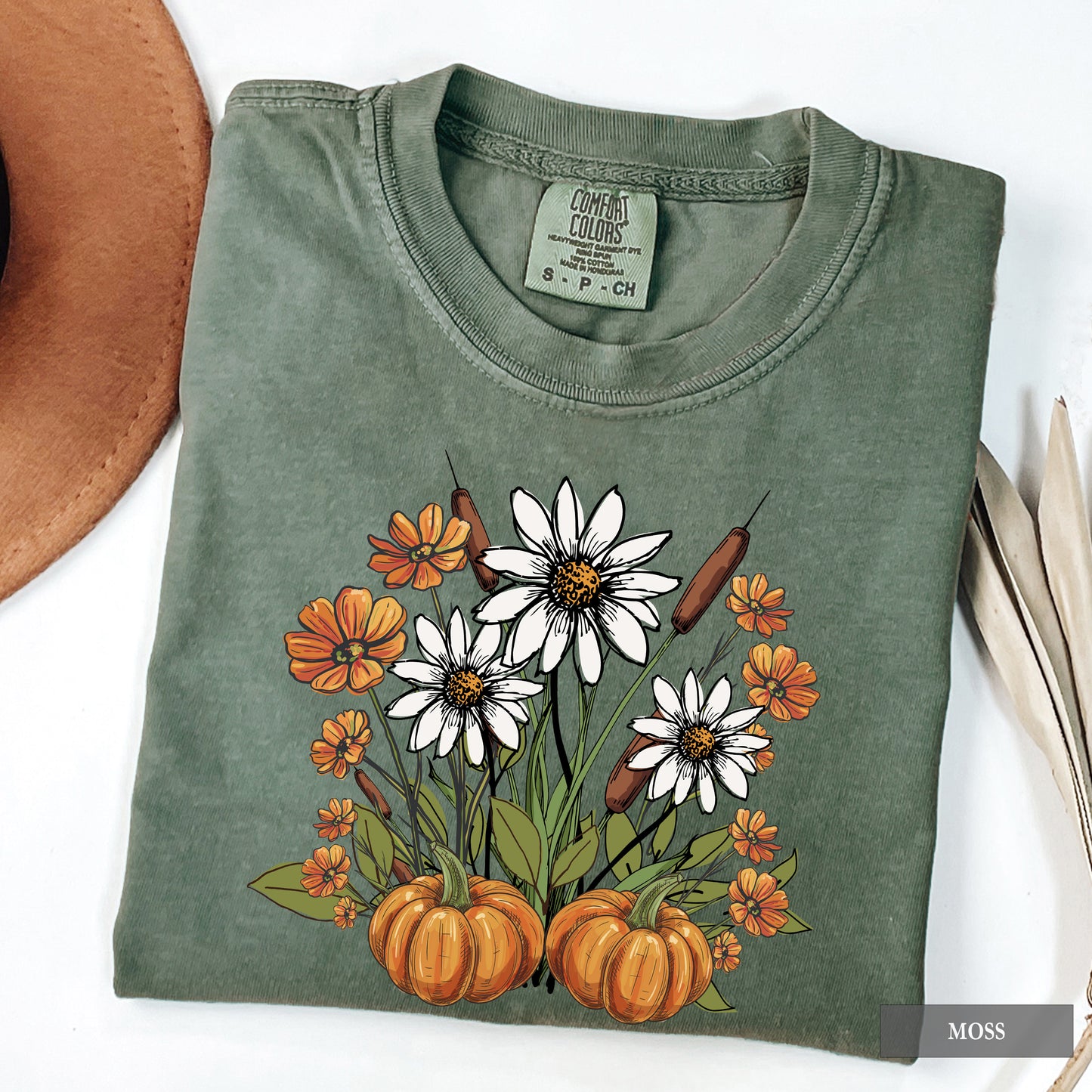 Folded green t-shirt with autumn-themed design featuring pumpkins and flowers on a white background.