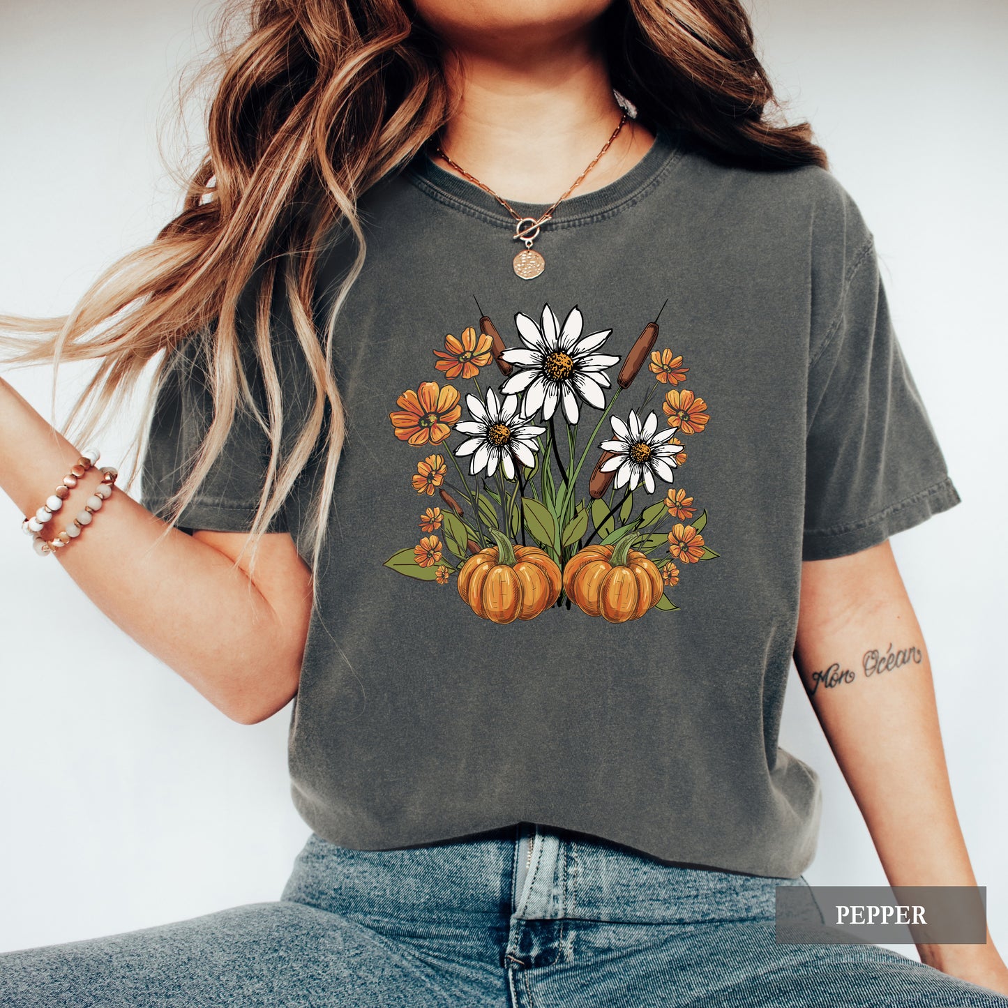 Person wearing a dark gray t-shirt with floral and pumpkin design, standing against a white background.