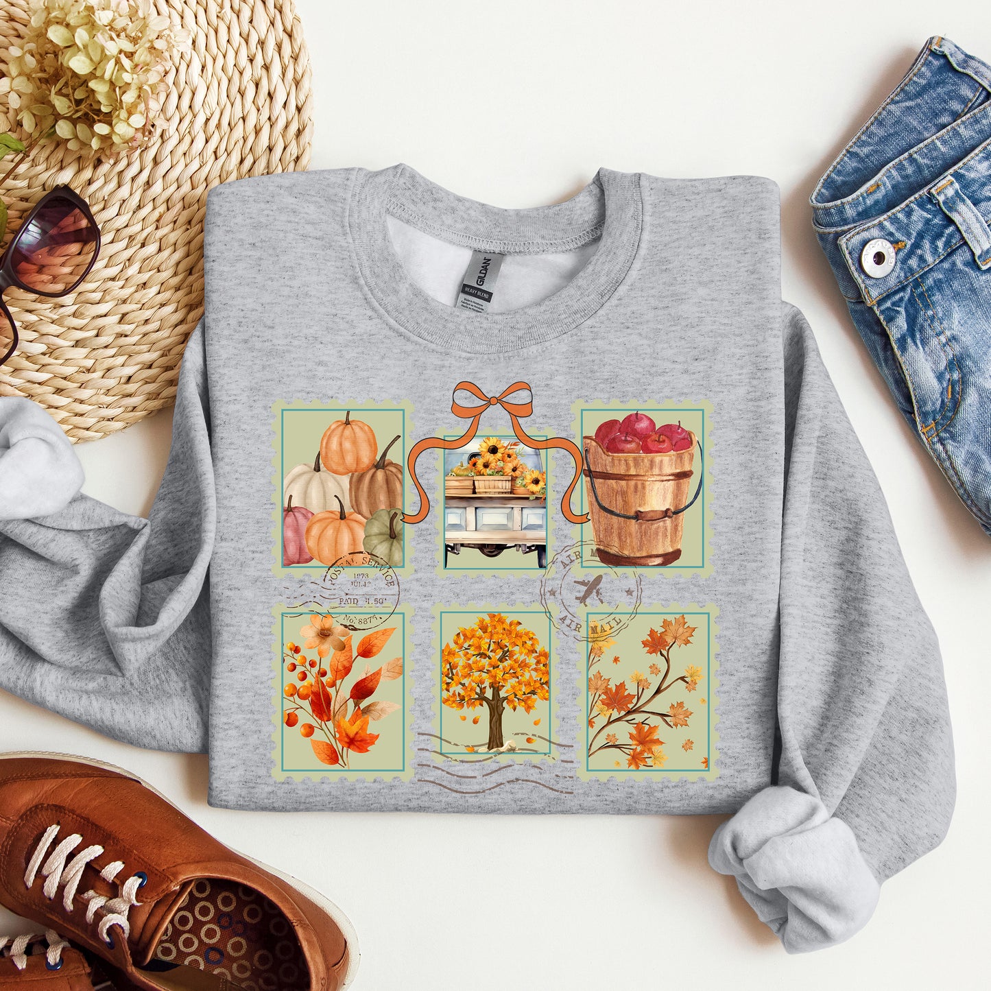 Gray sweatshirt with autumn-themed design on a white surface with accessories.