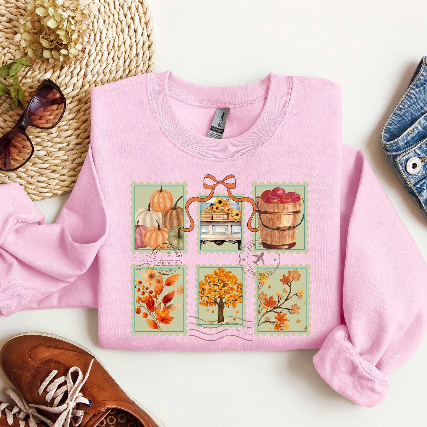 Pink sweatshirt with autumn-themed postage stamp design on a white surface with shoes and a bag.