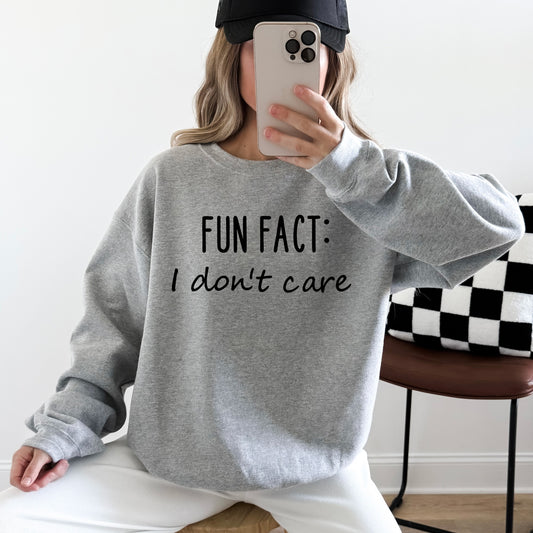 A woman wearing a heather grey sweatshirt that says 'Fun Fact: I don't care' on it.