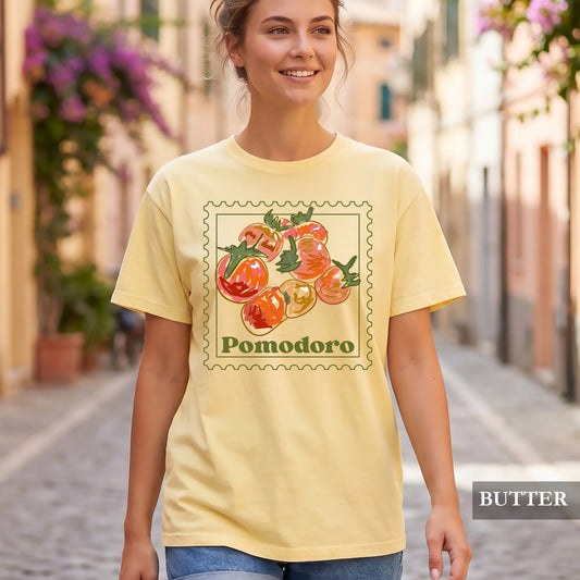 Woman wearing a yellow t-shirt with 'Pomodoro' design on a street with flowers.