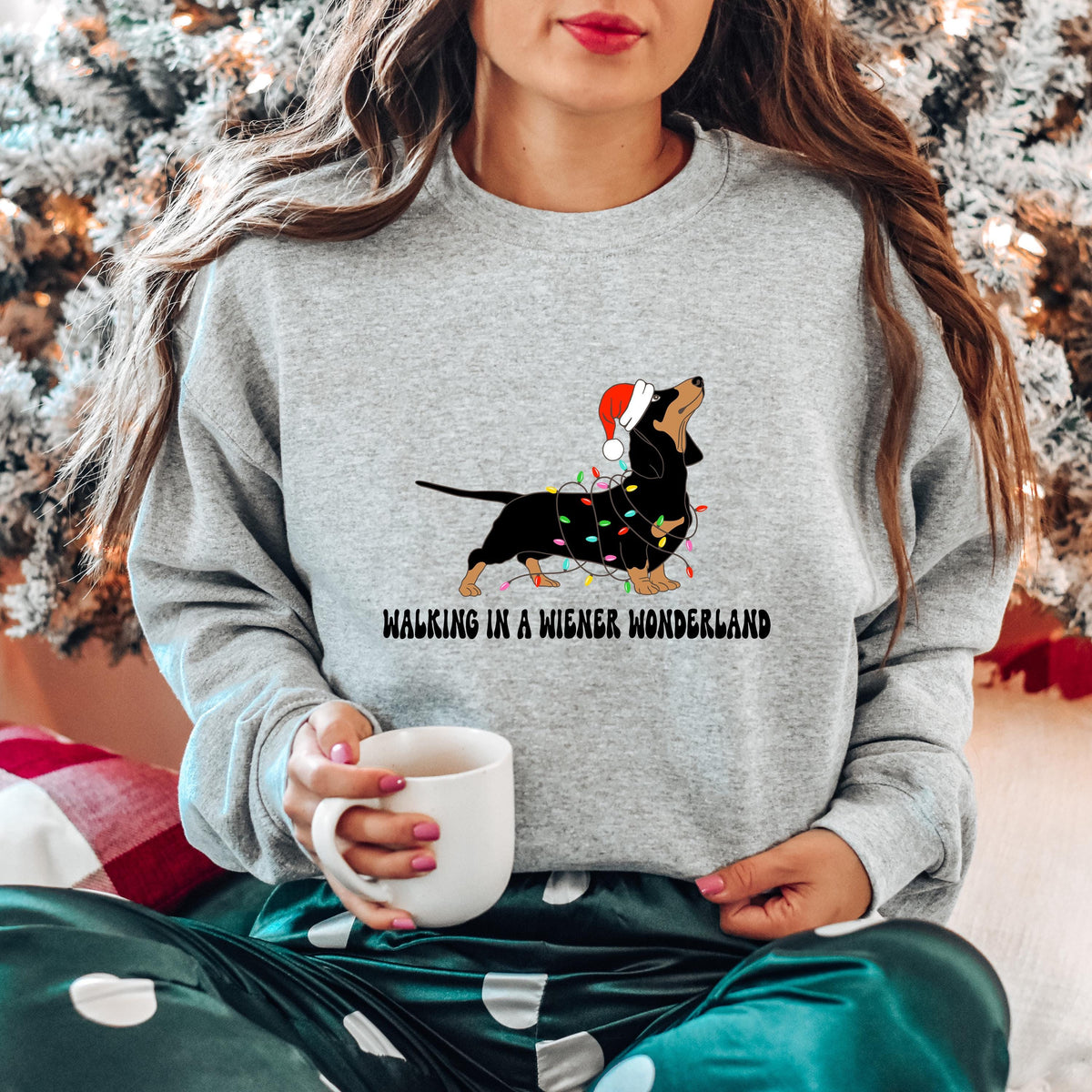 A sport grey Gildan sweatshirt with a picture of a dachshund tangled in christmas lights and wearing a santa hat.  Beneath the picture are the words, Walking in a Wiener Wonderland