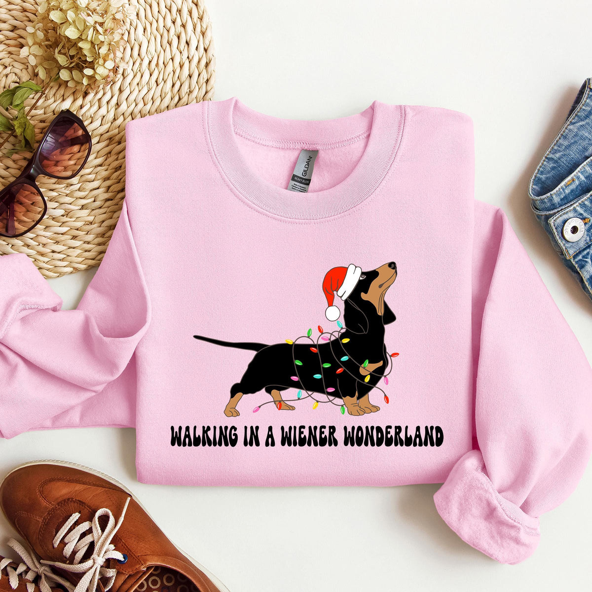 A pink Gildan sweatshirt with a picture of a dachshund tangled in christmas lights and wearing a santa hat.  Beneath the picture are the words, Walking in a Wiener Wonderland