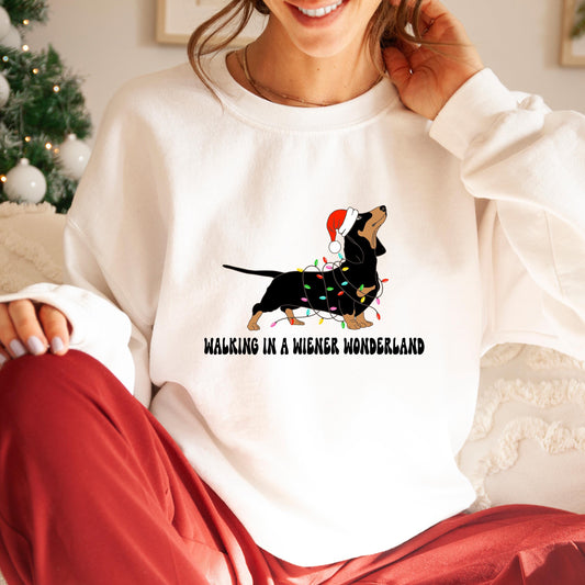 A white Gildan sweatshirt with a picture of a dachshund tangled in christmas lights and wearing a santa hat.  Beneath the picture are the words, Walking in a Wiener Wonderland
