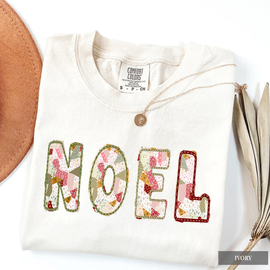 An ivory Comfort Colors shirt with NOEL on it in a sage green, maroon, and cream patchwork pattern.