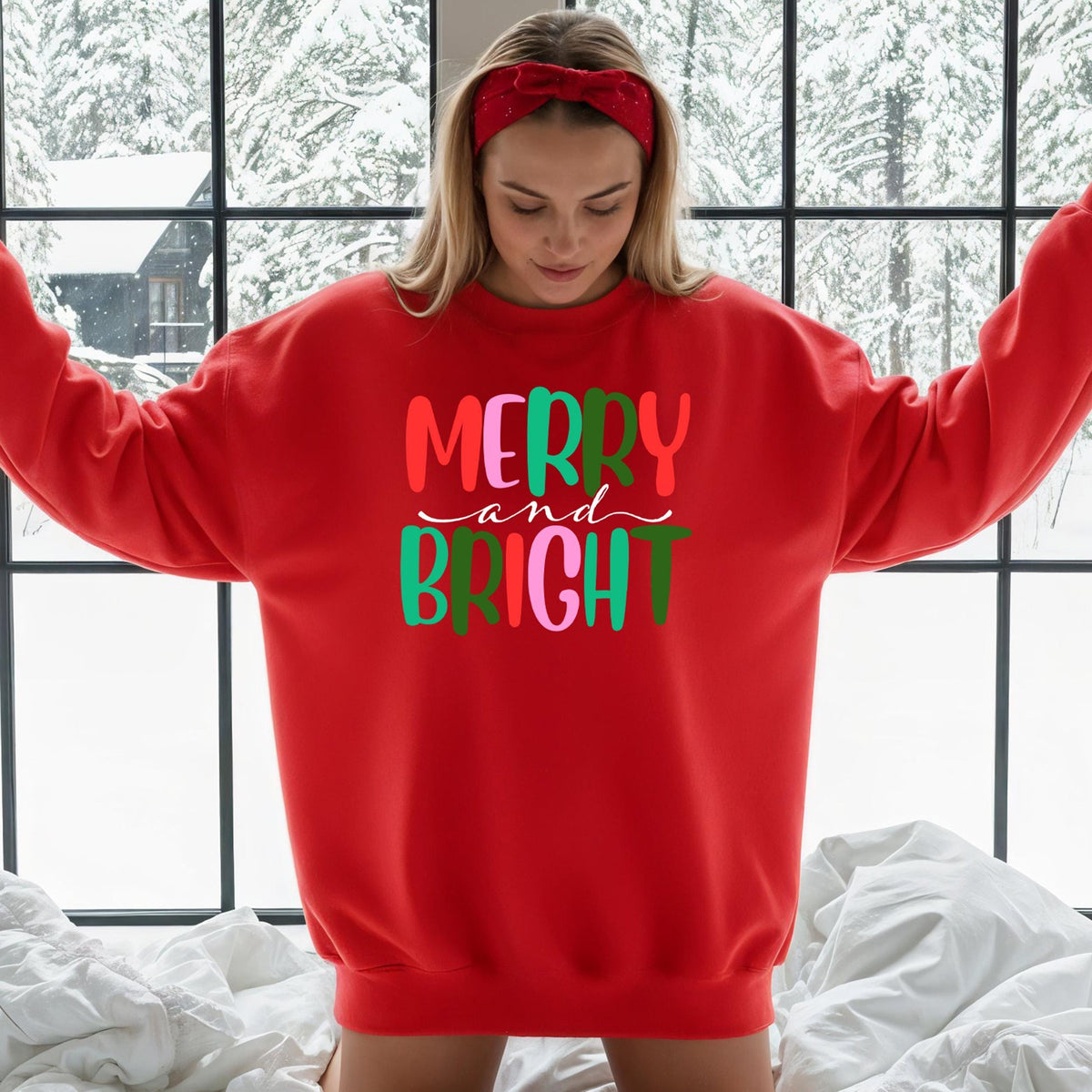 A red sweatshirt with colorful Merry and Bright text is displayed against a snowy window backdrop.