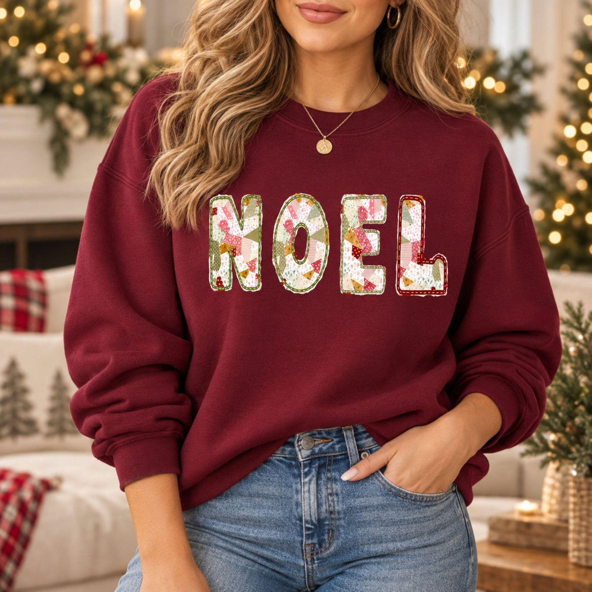 A woman wearing a maroon Gildan crewneck sweatshirt with NOEL printed on it in a muted sage, maroon, and white patchwork pattern.
