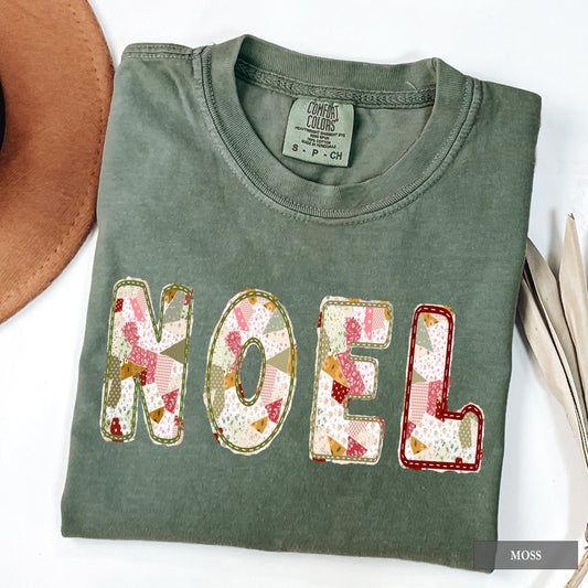 A moss Comfort Colors shirt with NOEL on it in a sage green, maroon, and cream patchwork pattern.