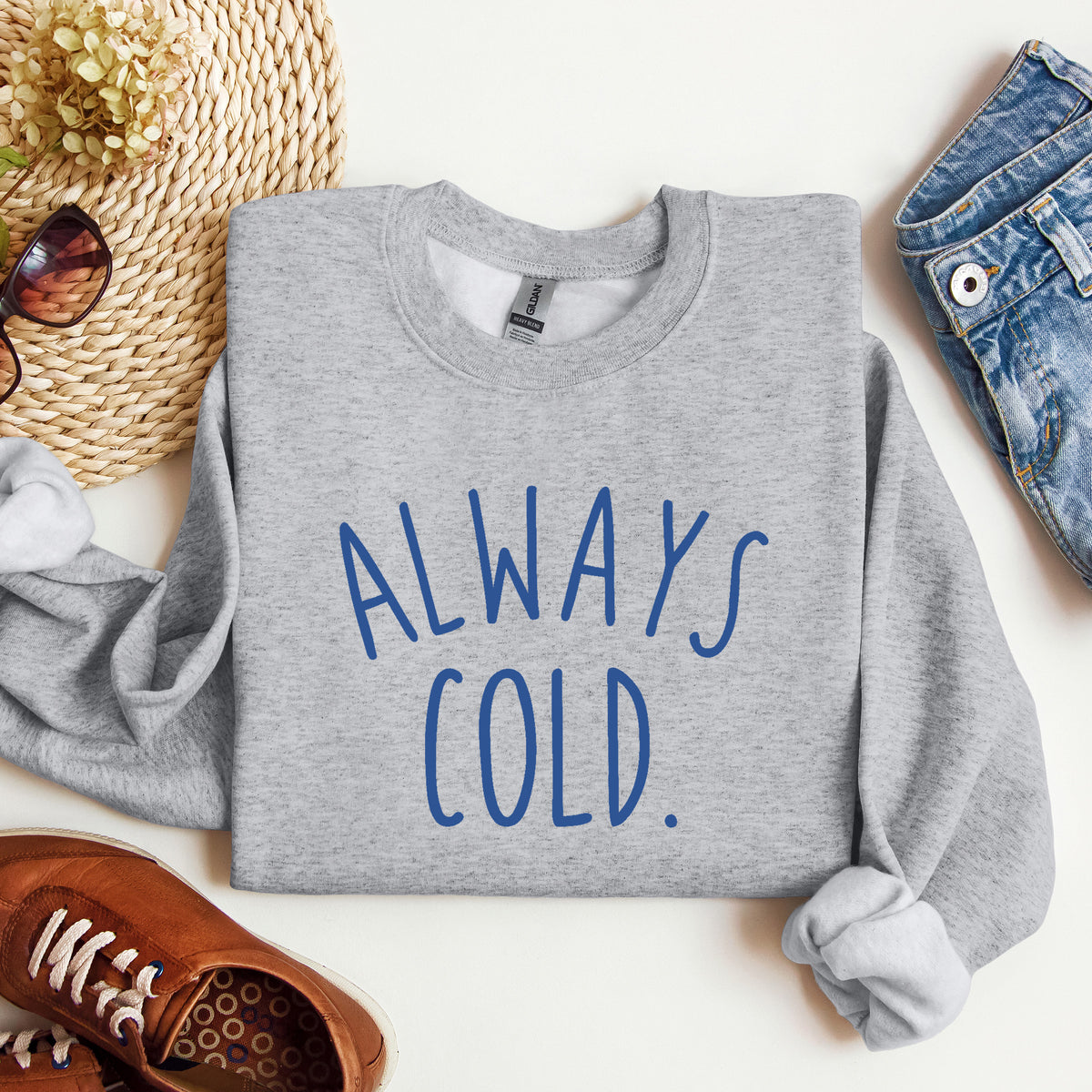 A heather gray crewneck sweatshirt with the text 'ALWAYS COLD.' printed in blue across the chest.