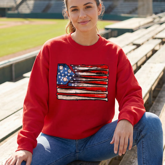 Woman wearing a red sweatshirt with an American flag design, sitting on bleachers at a baseball field.