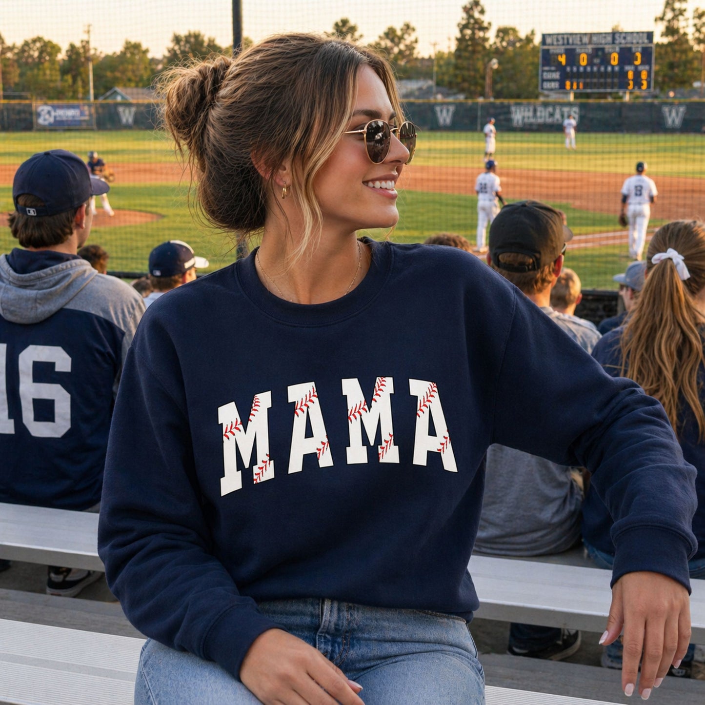 Woman wearing a navy sweatshirt with 'MAMA' and baseball graphics at a sports event.