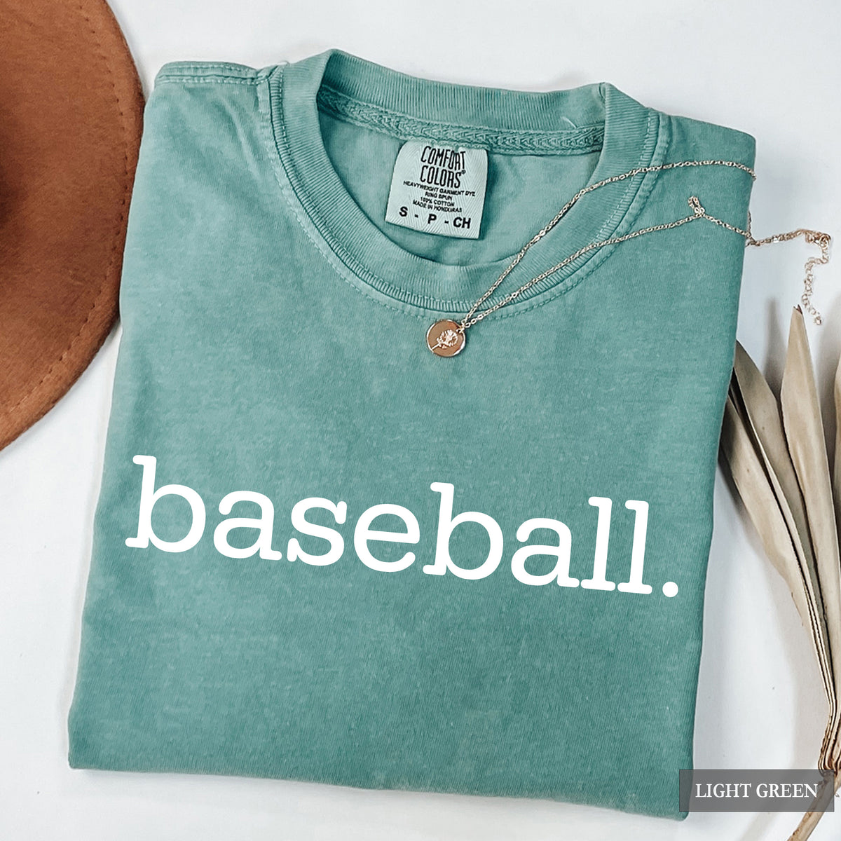 A folded light green t-shirt with the word 'baseball.' printed in white lowercase letters across the front.