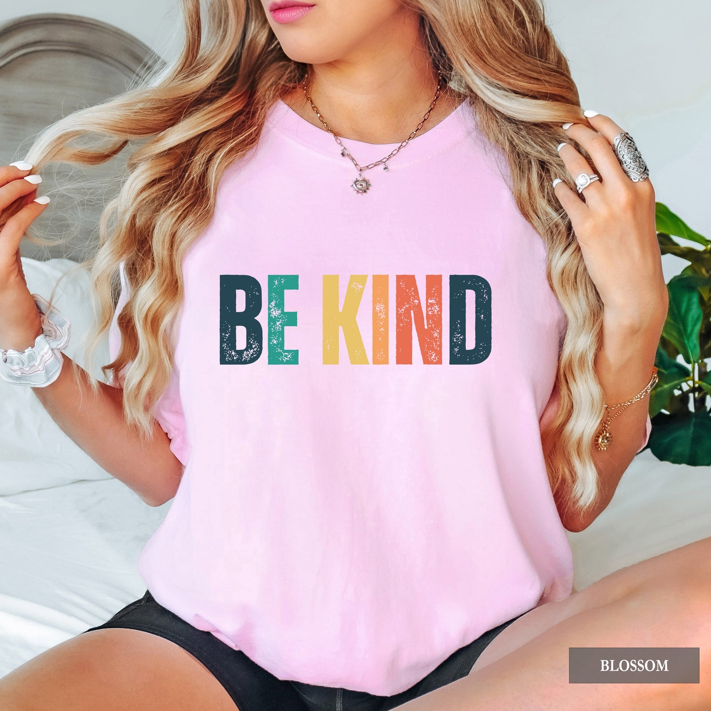 Person wearing a pink t-shirt with 'BE KIND' in colorful letters, sitting on a couch.