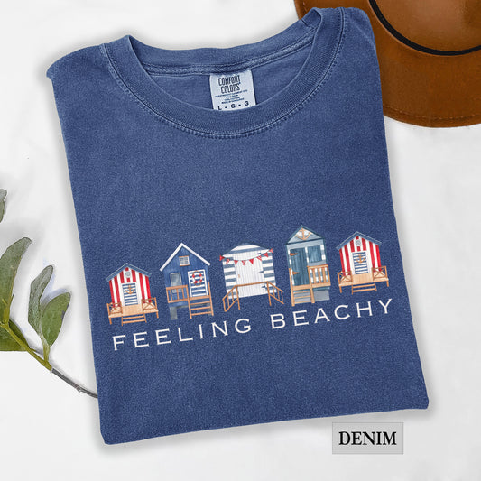 Folded denim blue t-shirt with beach hut design and 'Feeling Beachy' text on a white background.