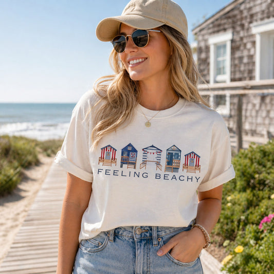 Woman wearing a 'Feeling Beachy' t-shirt with beach hut design by the ocean.
