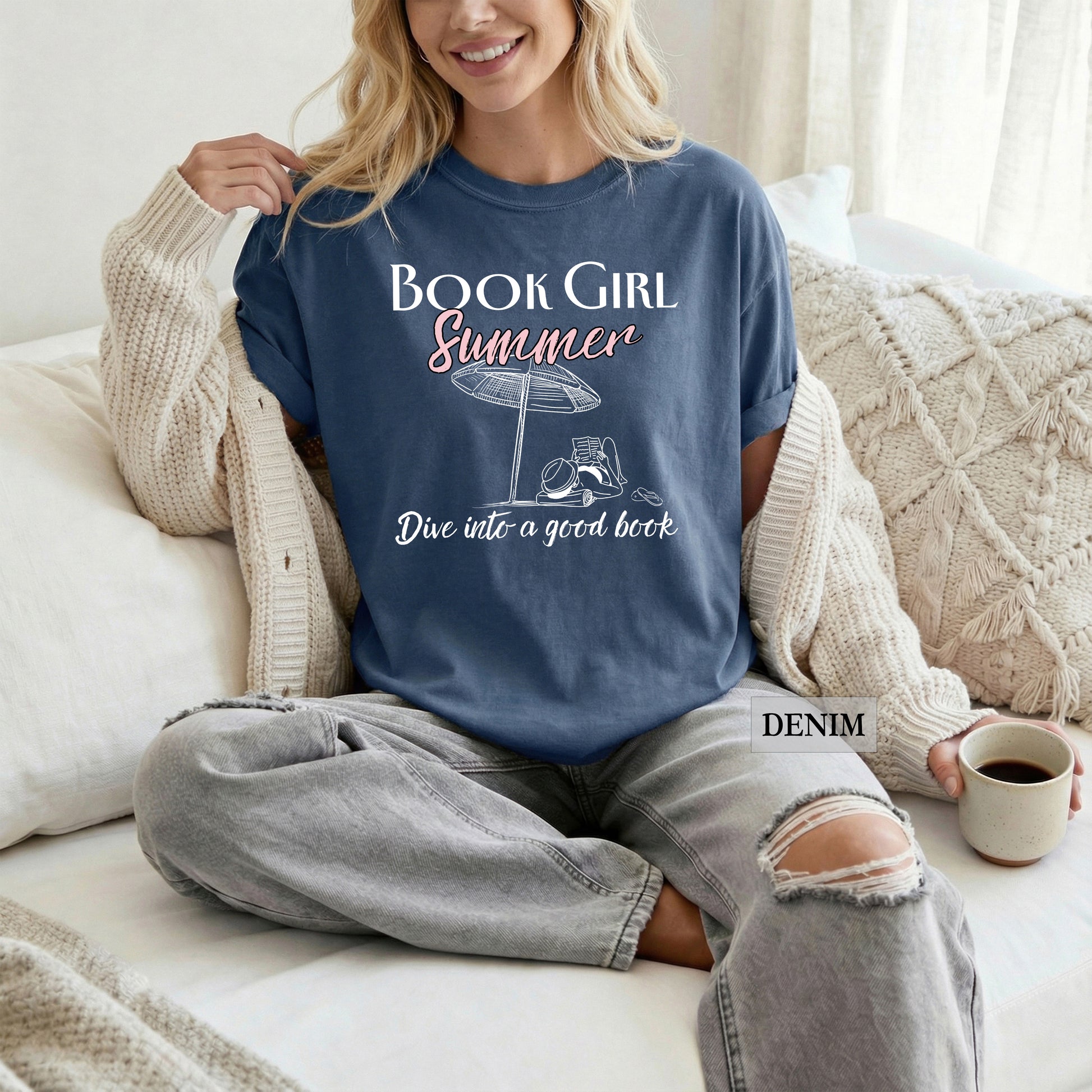 Woman wearing a 'Book Girl Summer' t-shirt sitting on a couch with a cup of coffee.