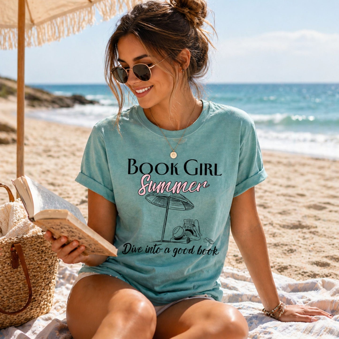 Woman on a beach wearing a 'Book Girl Summer' t-shirt, holding an open book.