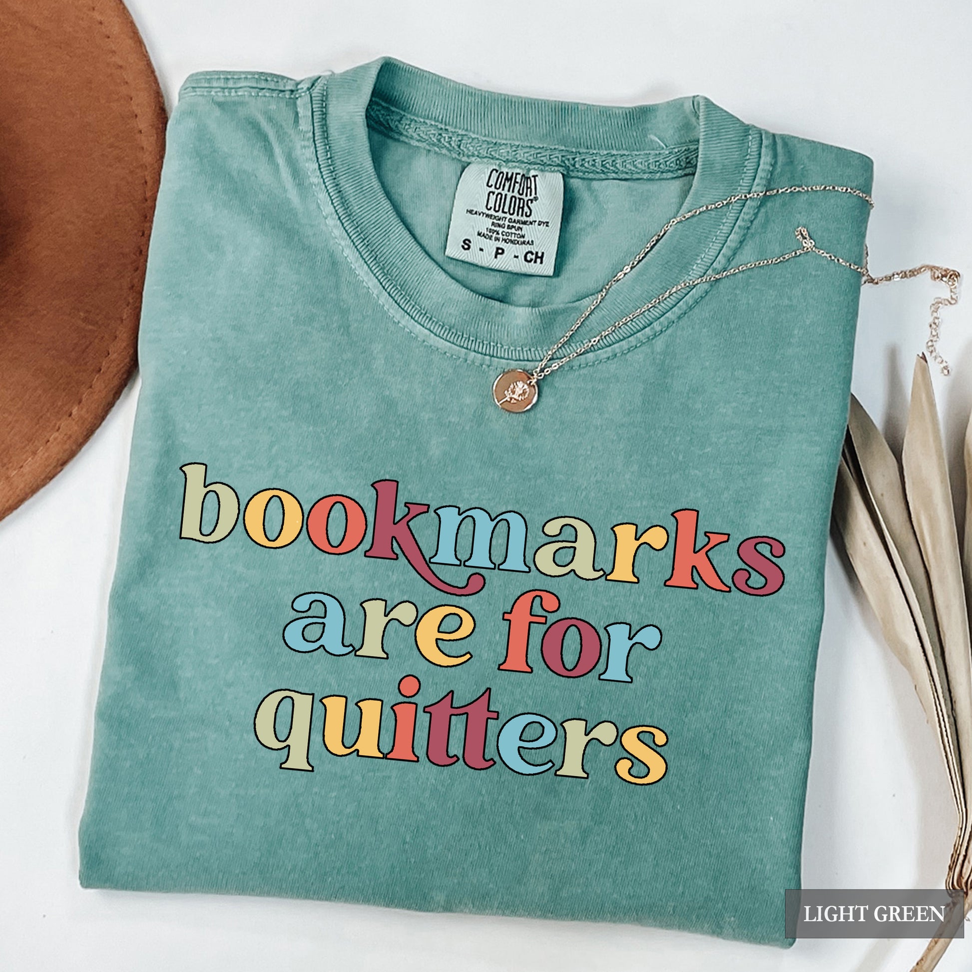 Light green t-shirt with colorful text 'bookmarks are for quitters' on a white background