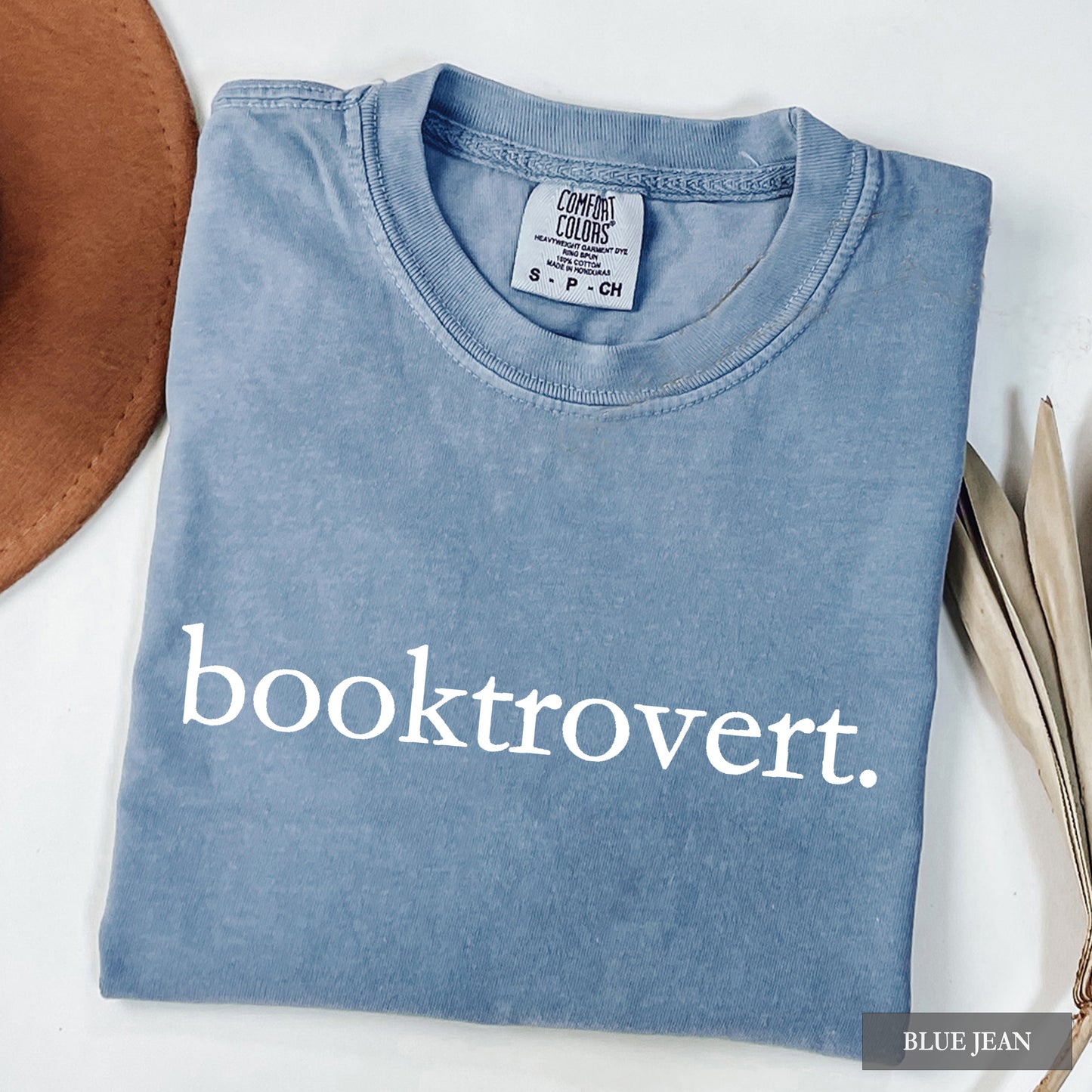A blue jean comfort colors shirt with "booktrovert" on the front in minimalist typewriter style font.