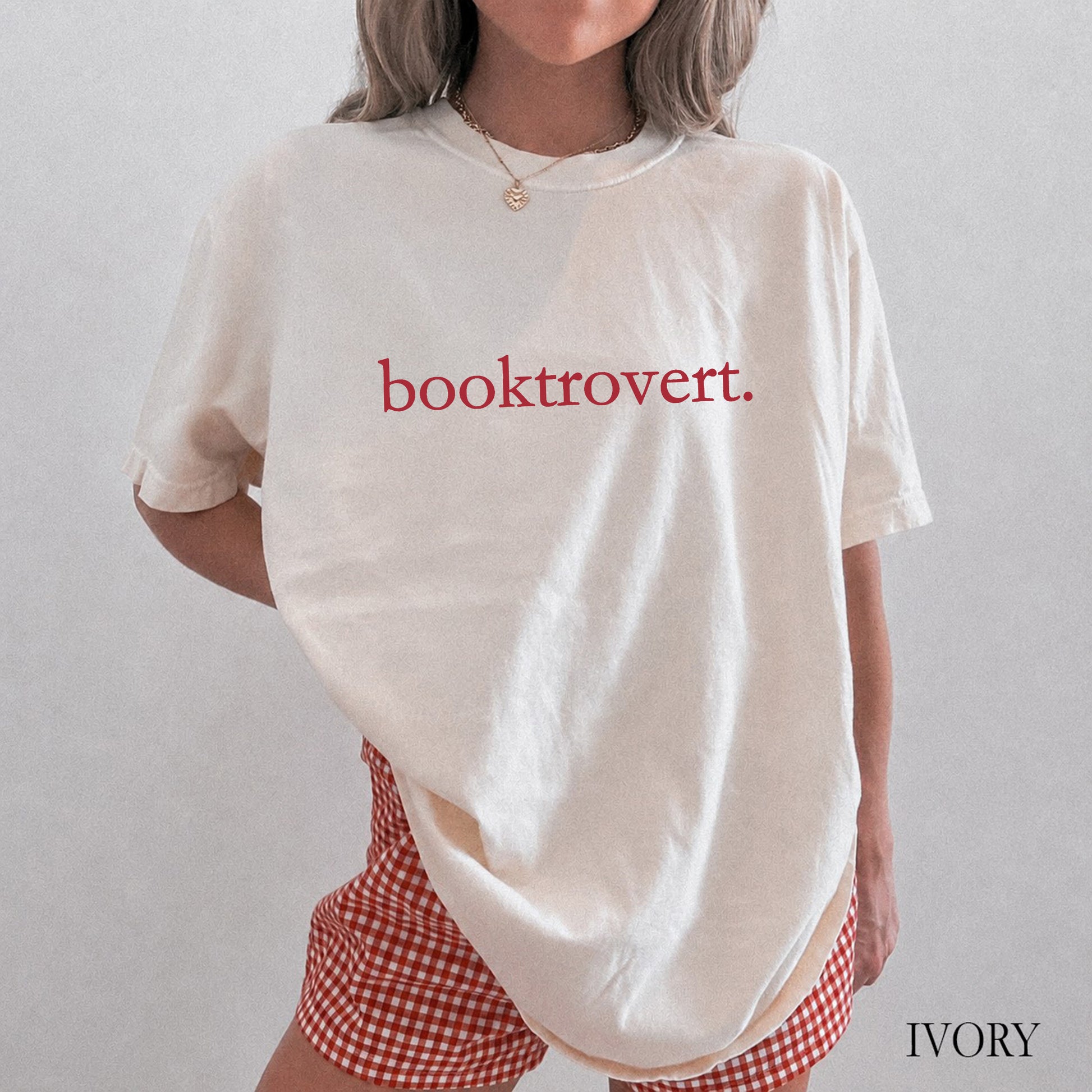 Woman wearing an ivory comfort colors shirt with "booktrovert" on the front in minimalist typewriter style font.