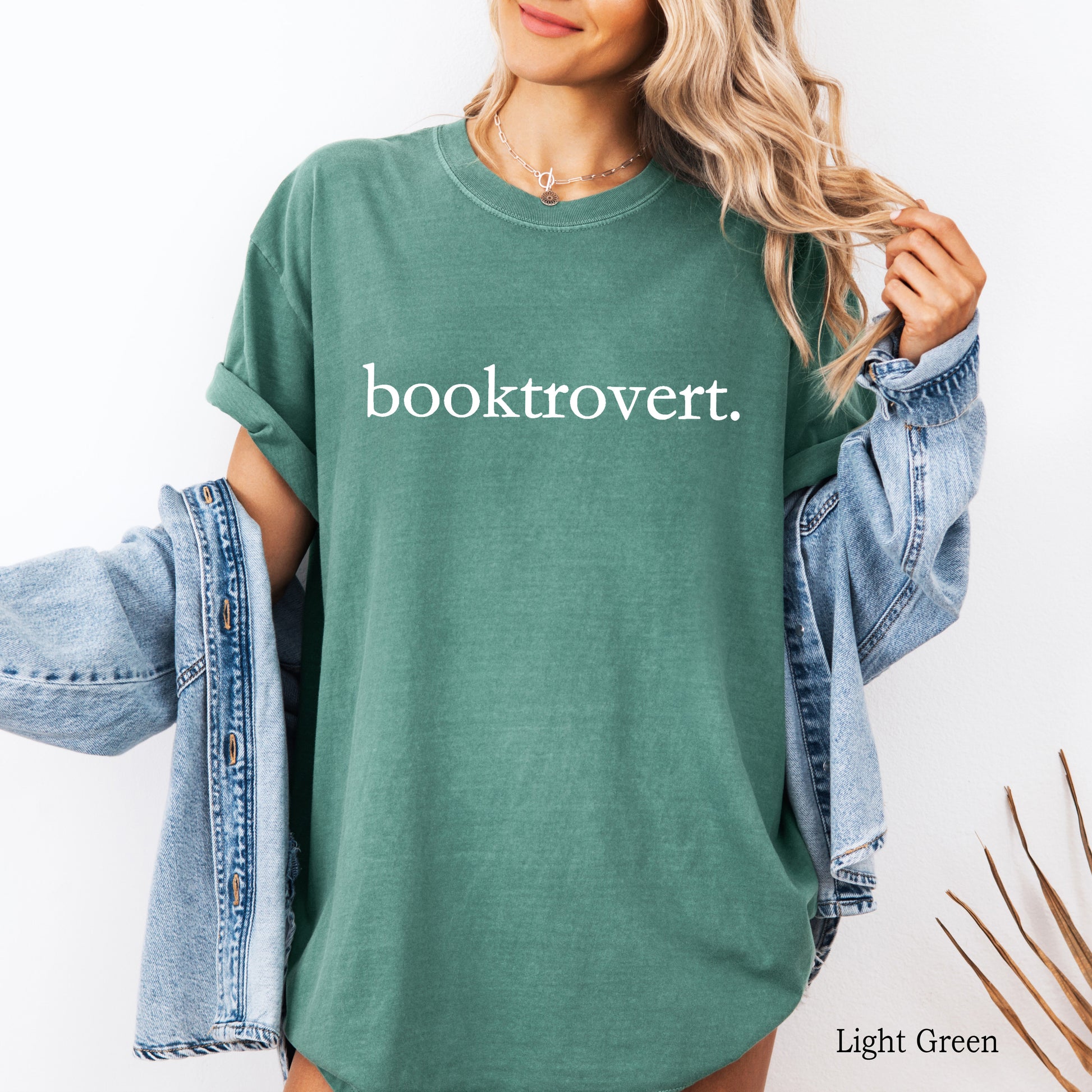 Woman wearing a light green comfort colors shirt with "booktrovert" on the front in minimalist typewriter style font.
