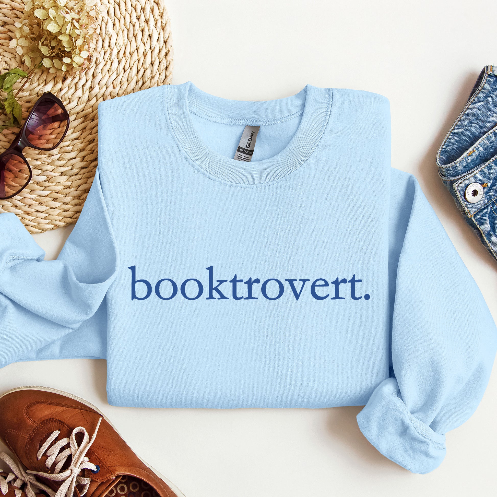 Woman wearing a light blue Gildan sweatshirt with 'booktrovert' on it in minimalist typewriter style font.