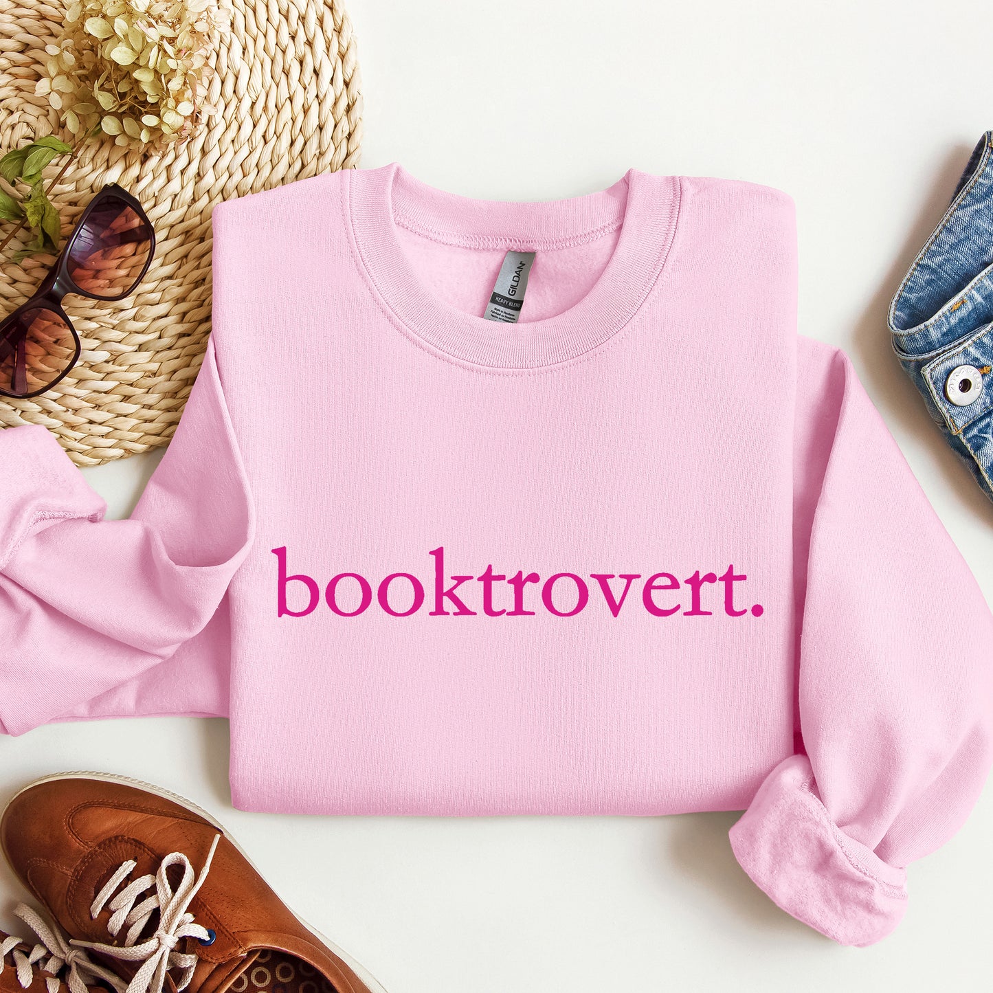 A Light Pink Gildan sweatshirt with 'booktrovert' on it in minimalist typewriter style font.