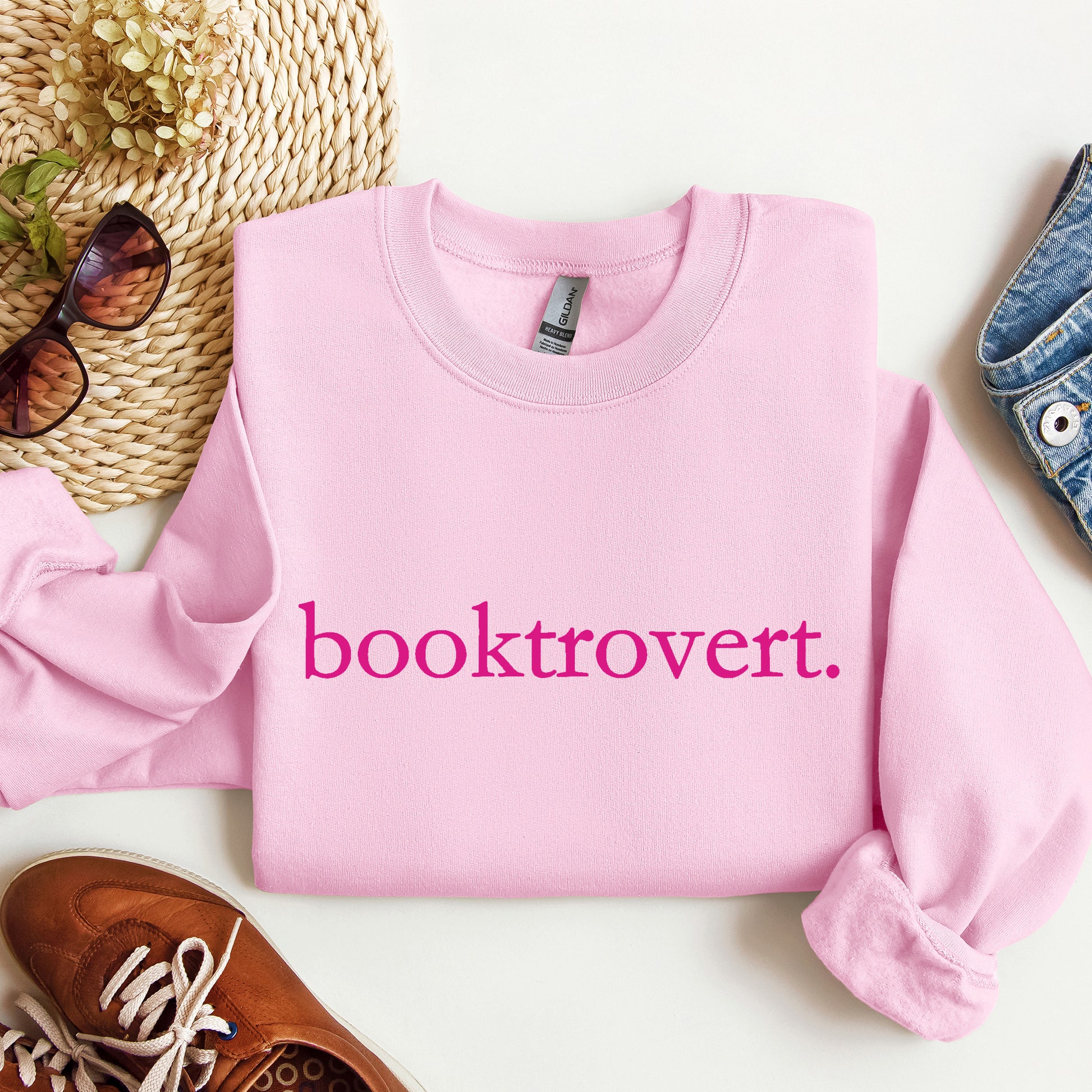 A Light Pink Gildan sweatshirt with 'booktrovert' on it in minimalist typewriter style font.