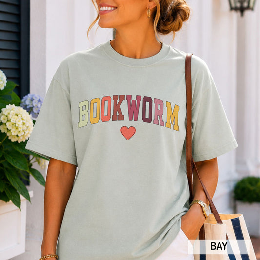 Woman wearing a 'BOOKWORM' t-shirt with colorful text and a heart, standing outdoors.
