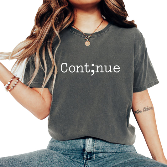 A woman wearing a dark gray mineral-wash t-shirt with the word 'Continue' printed in white text, paired with blue jeans against a solid white background.