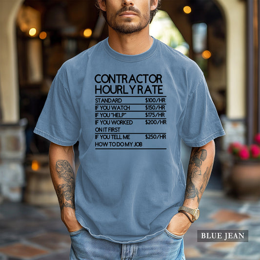 A man wearing a light blue graphic t-shirt with a humorous 'Contractor Hourly Rate' table printed in black. The background is a softly blurred outdoor patio setting.