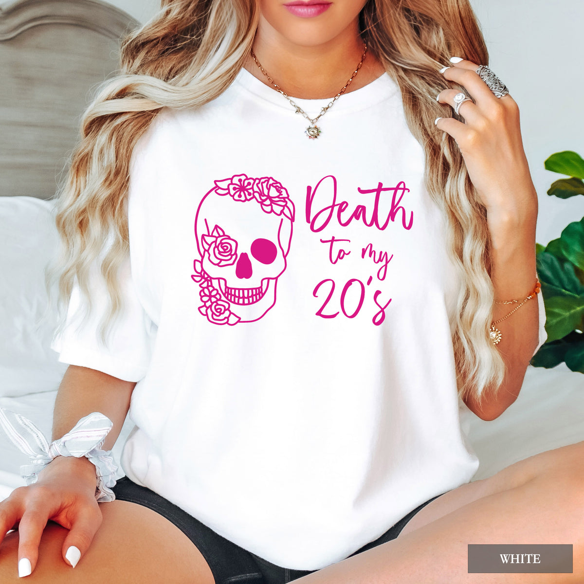 A woman wearing a white short-sleeve t-shirt with a pink graphic of a floral sugar skull and the text 'Death to my 20's'.