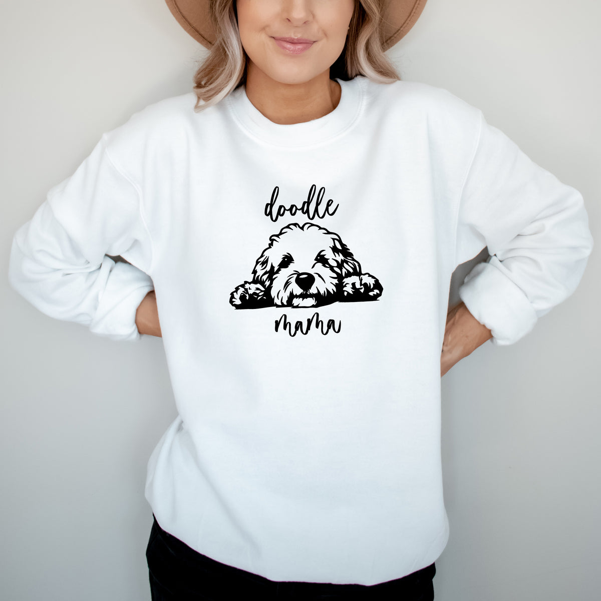 A woman wearing a white sweatshirt with 'doodle mama' and a picture of a goldendoodle on it.
