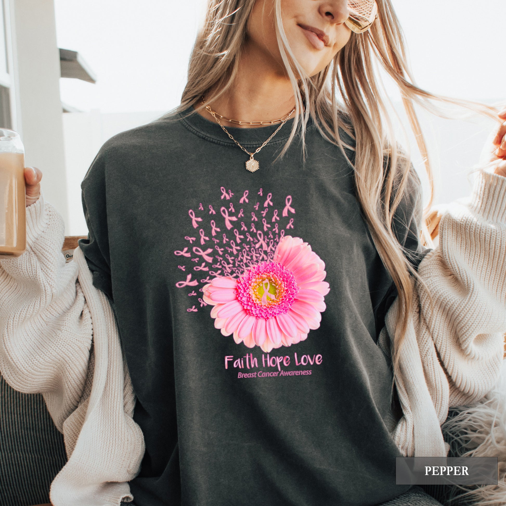 Person wearing a dark gray sweatshirt with a pink breast cancer awareness flower and 'Faith Hope Love' text, surrounded by neutral-colored clothing.