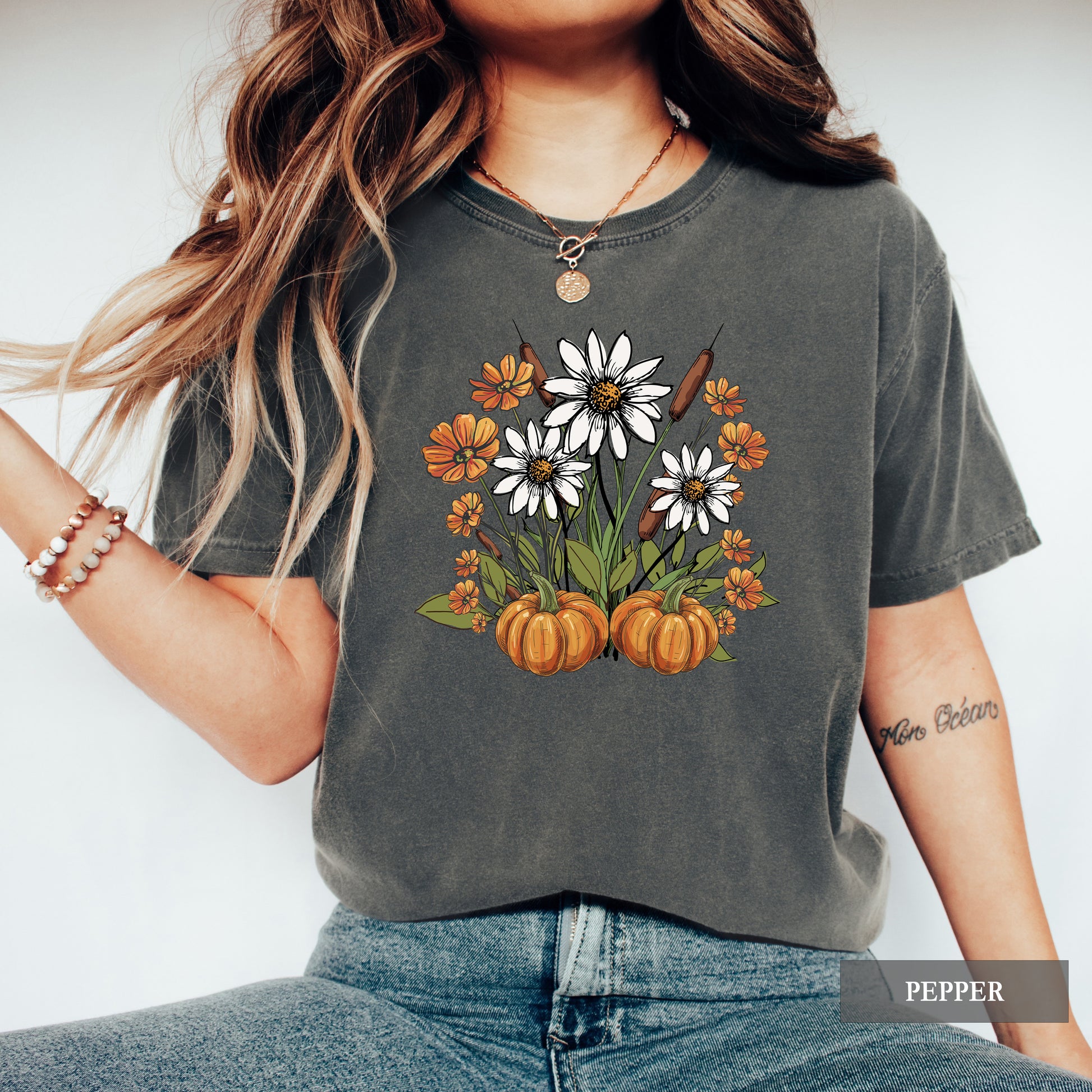 Person wearing a dark gray t-shirt with floral and pumpkin design, standing against a white background.