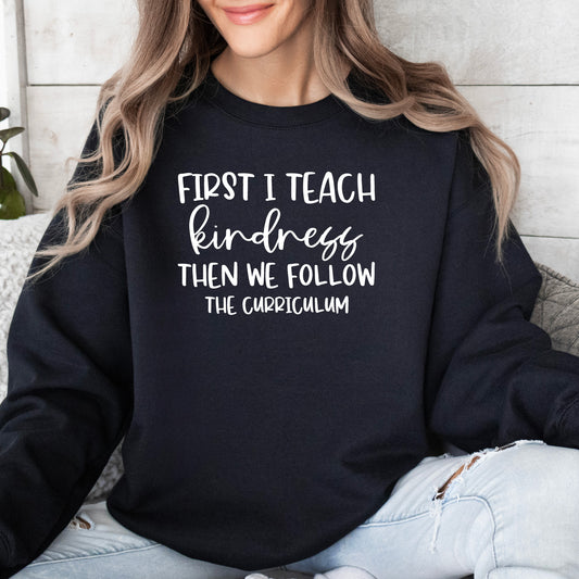 A black Gildan sweatshirt with First I Teach Kindness Then We Follow The Curriculum on it.