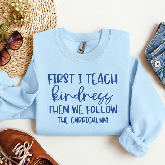 A light blue Gildan sweatshirt with First I Teach Kindness Then We Follow The Curriculum on it.