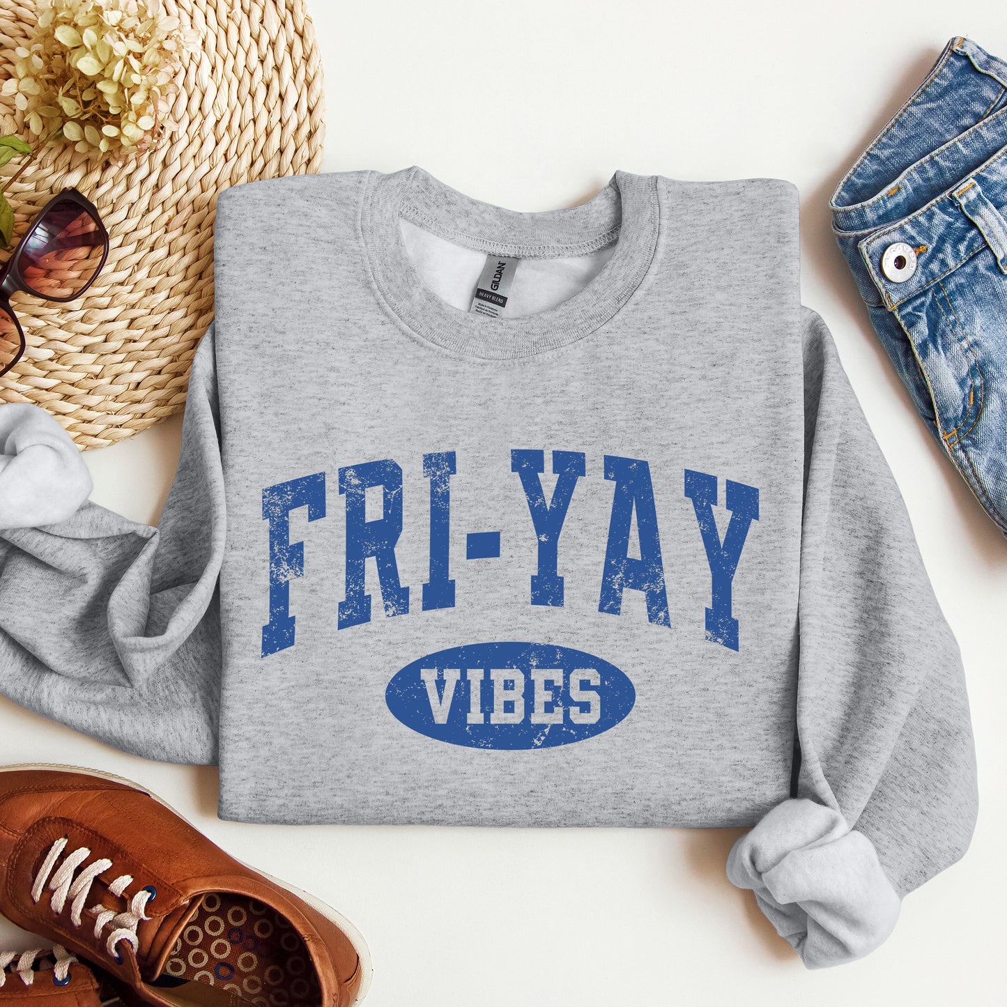 Gray sweatshirt with 'Fri-Yay Vibes' text on a white surface with accessories.