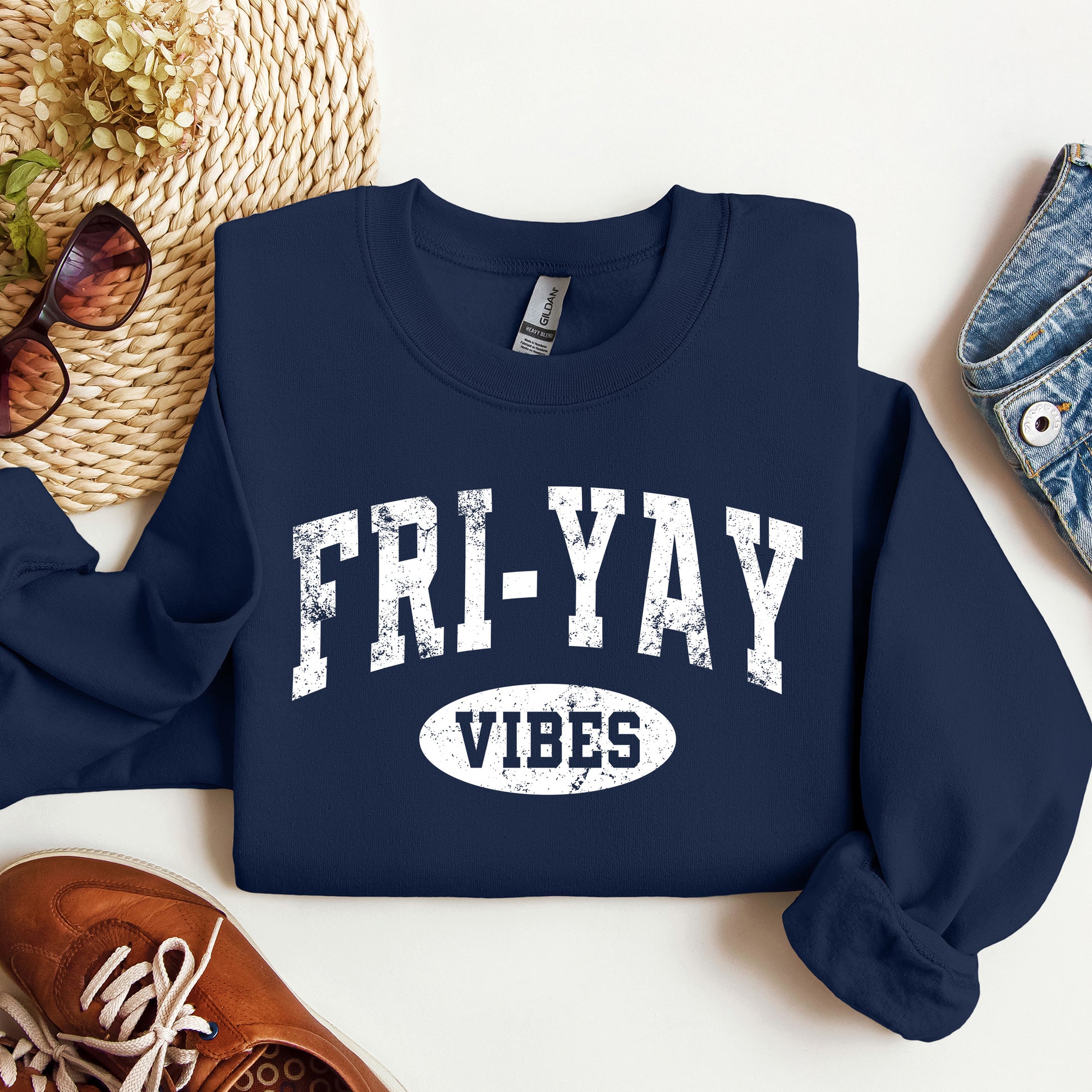 Navy blue sweatshirt with 'FRI-YAY VIBES' text on a white surface with accessories.