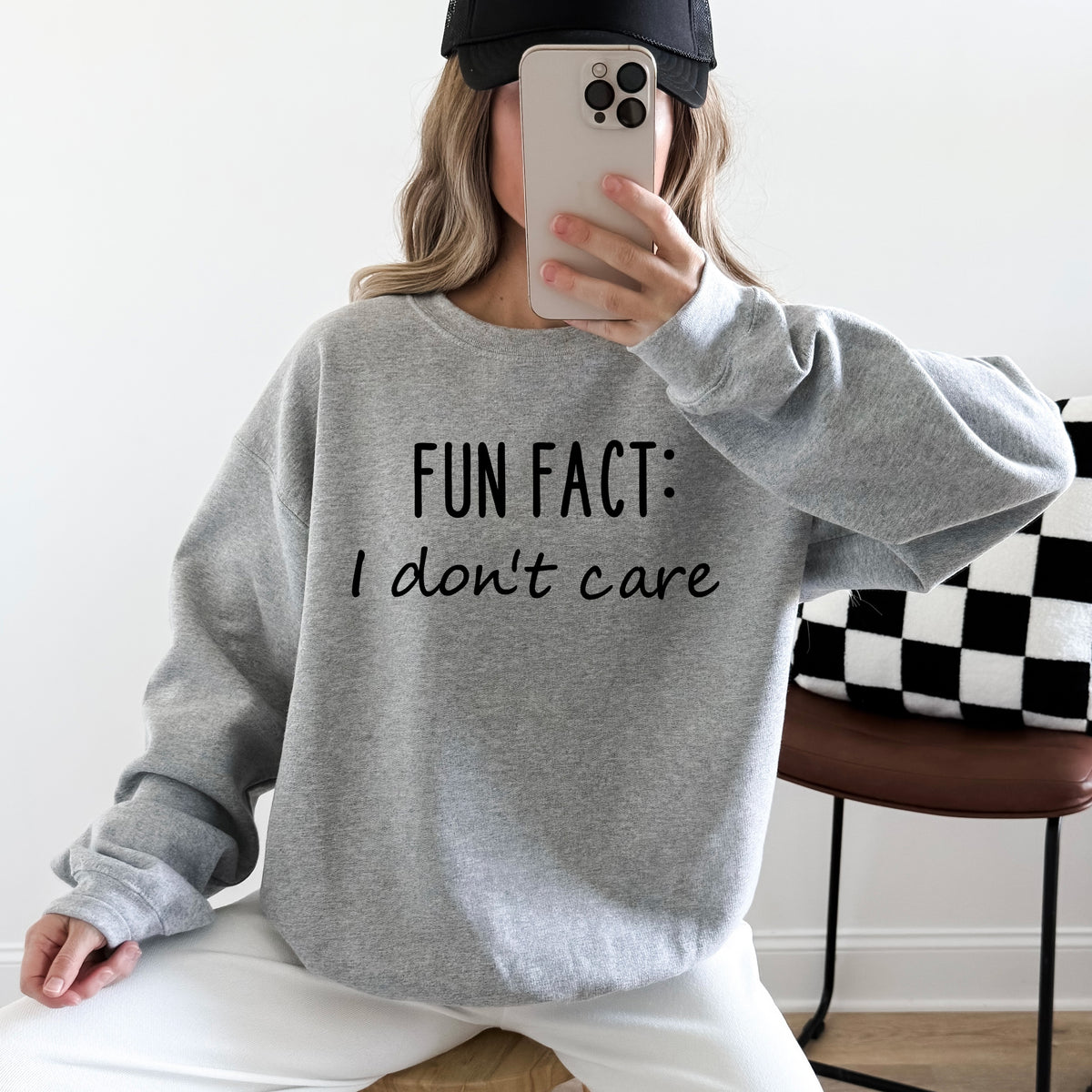 A woman wearing a heather grey sweatshirt that says 'Fun Fact: I don't care' on it.