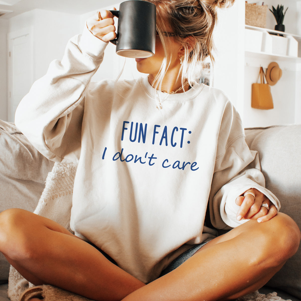 A woman wearing a sand sweatshirt that says 'Fun Fact: I don't care' on it.