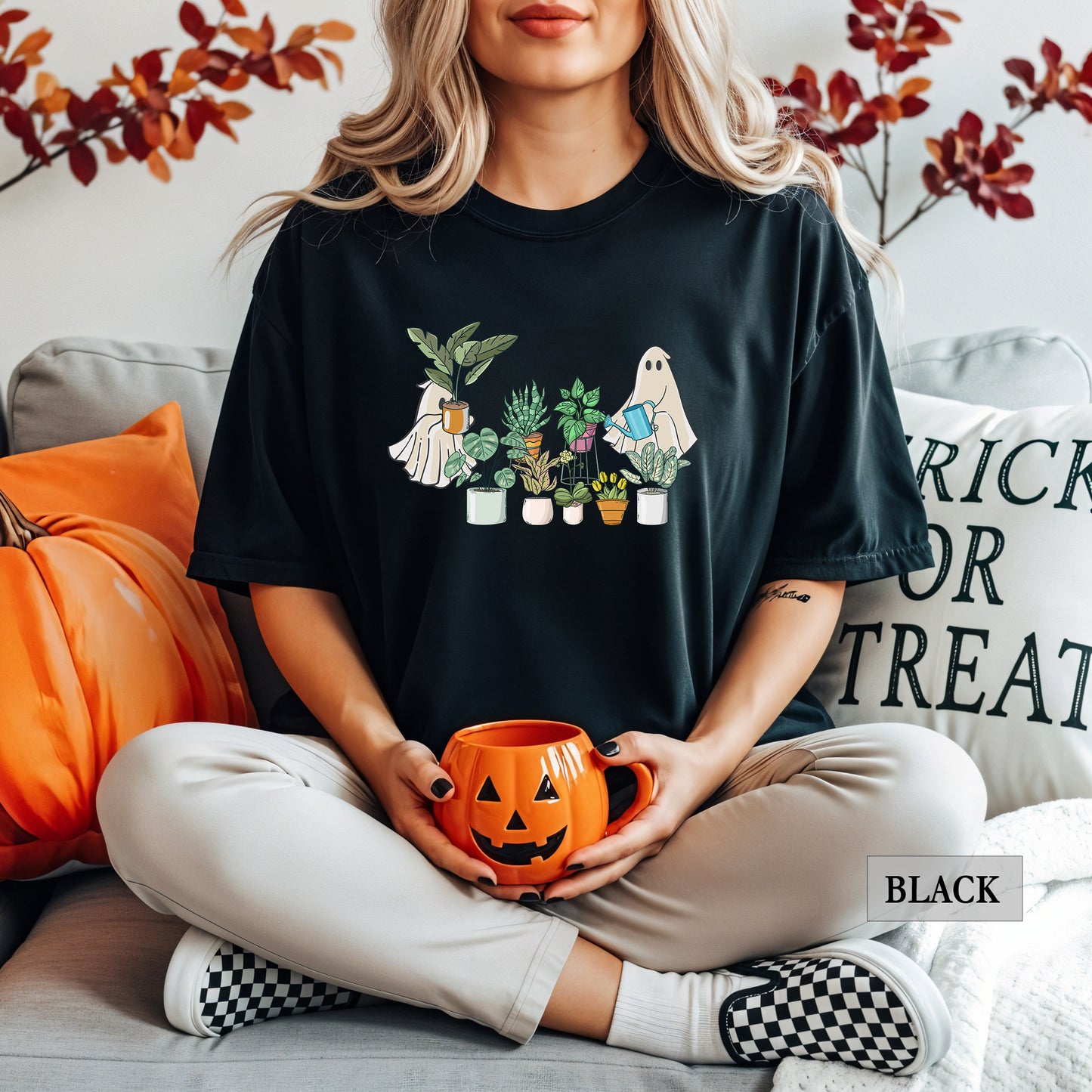 A woman wearing a black comfort colors t-shirt with ghosts tending to houseplants on it.