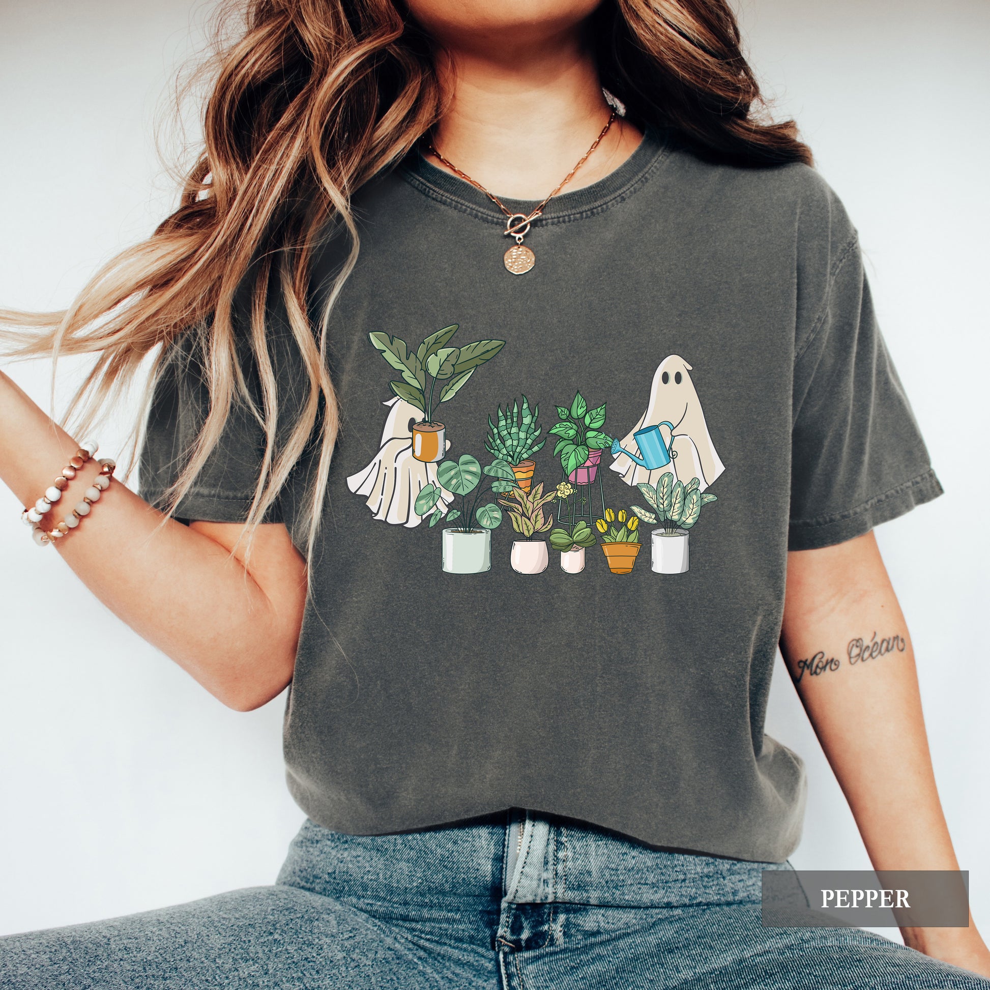 A woman wearing a pepper comfort colors t-shirt with ghosts tending to houseplants on it.