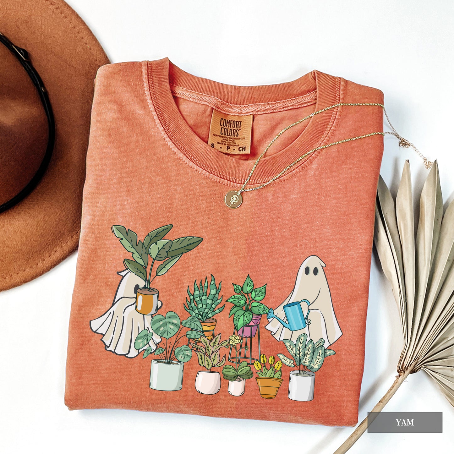 A woman wearing a yam comfort colors t-shirt with ghosts tending to houseplants on it.