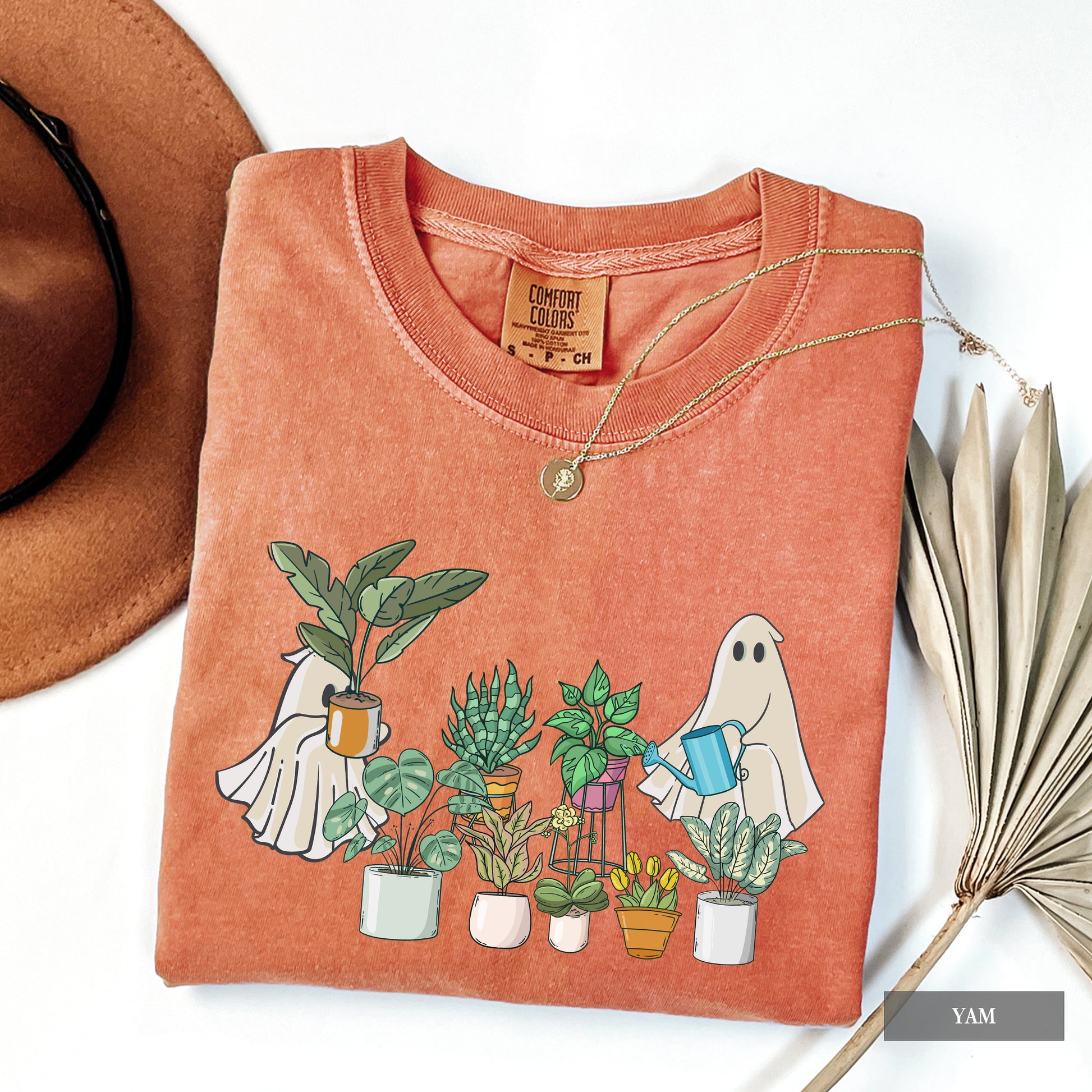 A woman wearing a yam comfort colors t-shirt with ghosts tending to houseplants on it.