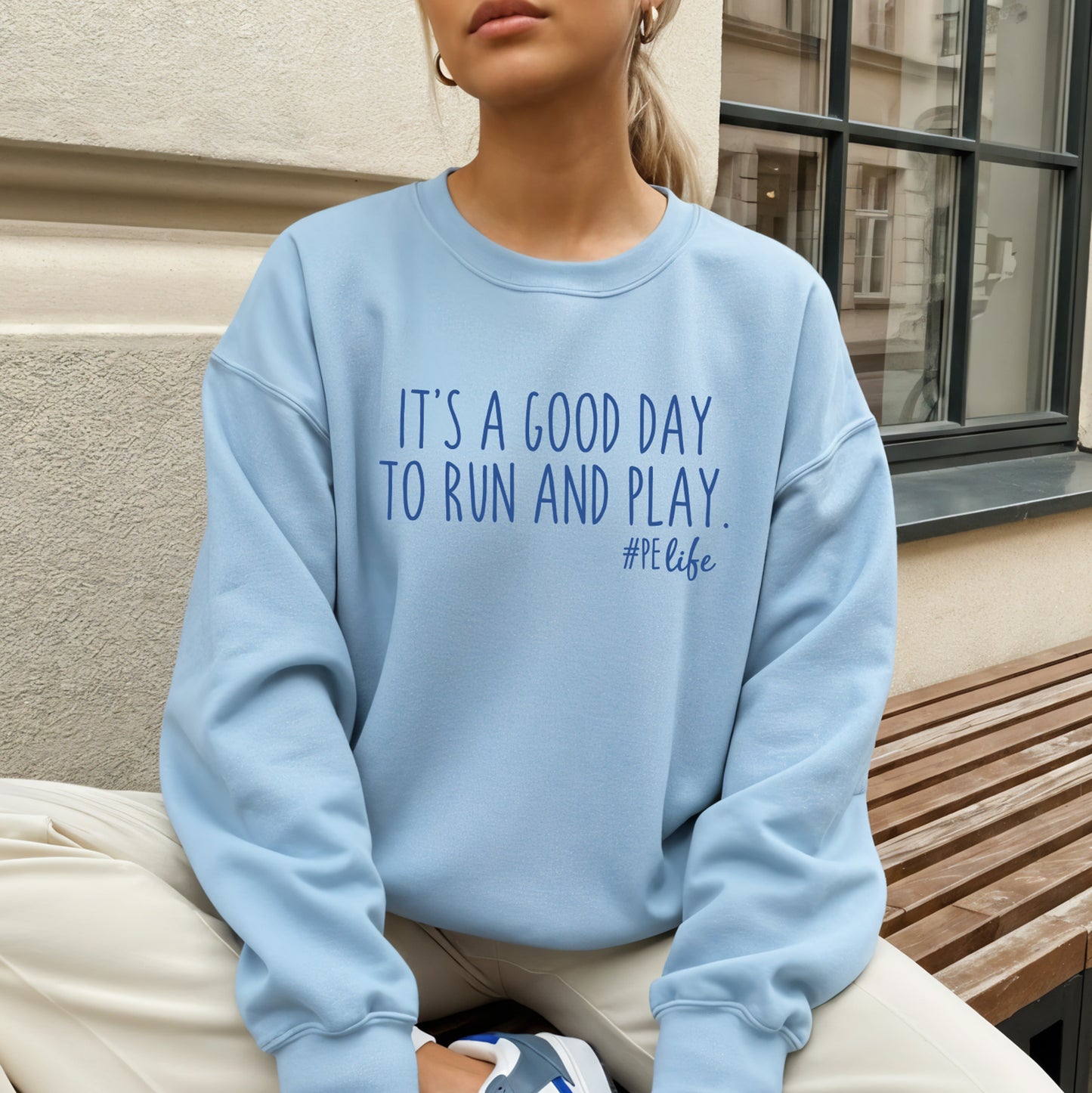 Woman wearing a light blue Gildan sweatshirt that says It's a Good Day to Run and Play #PE life